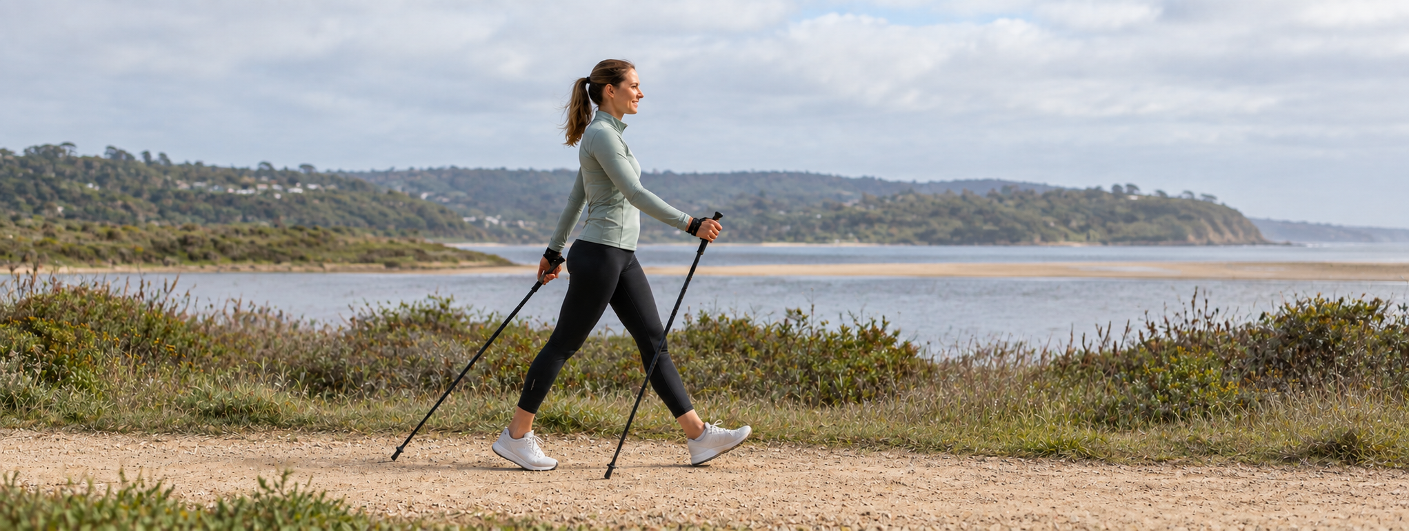 A woman Nordic Walking with pole gloves along a coastal lagoon path